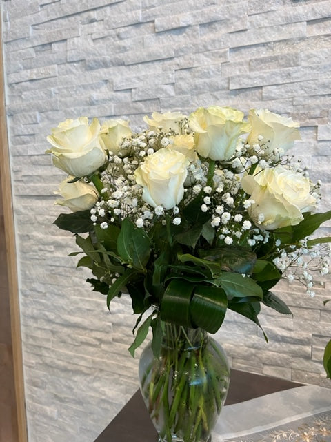 A bouquet of white roses arranged in a clear glass vase with green leaves.