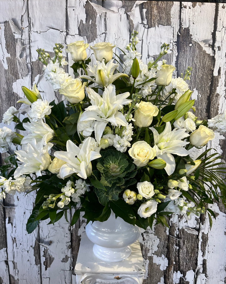 A white floral arrangement featuring roses and other flowers, displayed in a vase against a rustic wooden backdrop.