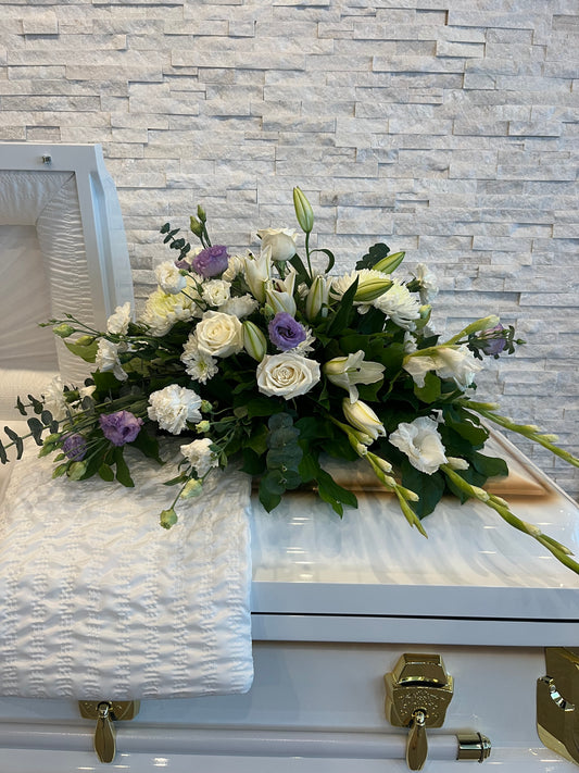 White and lavender casket spray with roses, lilies and fresh greenery arranged on a white casket