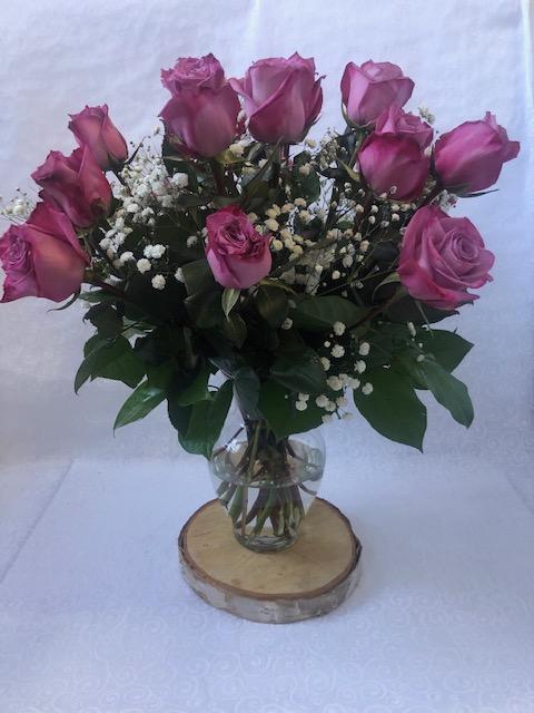 A bouquet of purple roses arranged in a clear vase, placed on a wooden surface.
