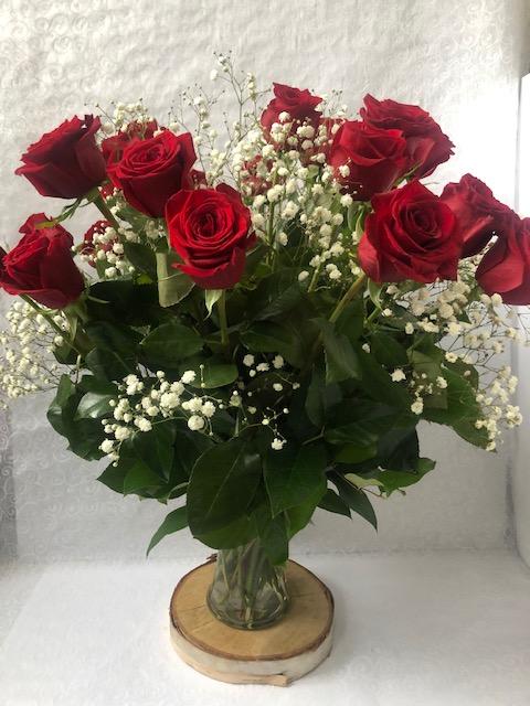 A dozen red roses and baby's breath arranged in a clear glass vase, placed on a wooden surface.