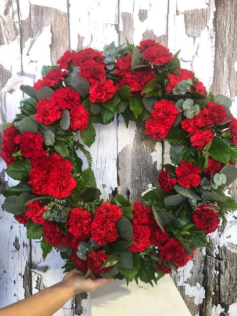 Red carnation funeral wreath with greenery by La Quenouille in Montreal