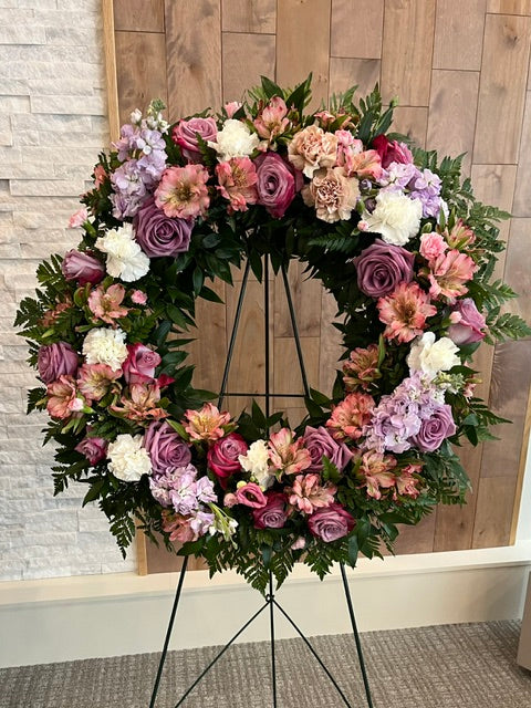 Soft pink and mauve funeral wreath with roses, carnations, and seasonal flowers