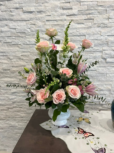 Soft pink rose sympathy arrangement with white flowers and greenery in a pedestal vase