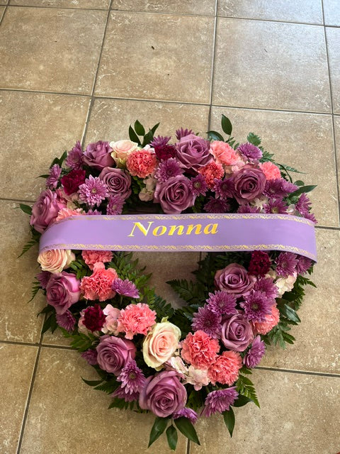 Floral wreath with pink and purple flowers and a purple ribbon on a tiled floor.